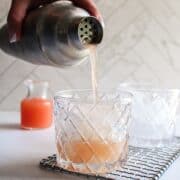 a grapefruit cocktail being poured out of a cocktail shaker into a glass