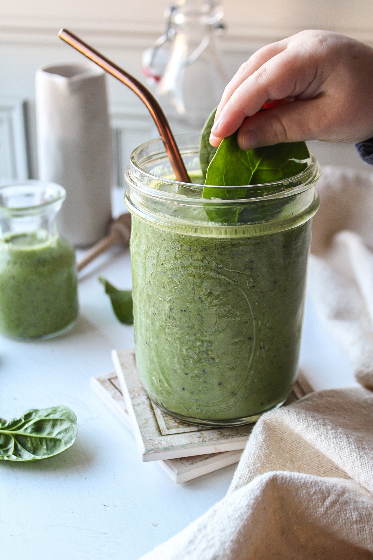 a green smoothie with a small hand holding a piece of spinach inserting into the smoothie