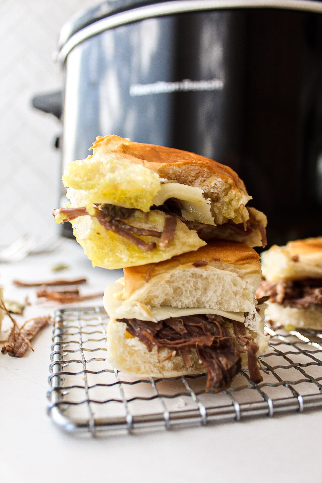 a stack of two pot roast sliders with a slow cooker in the background