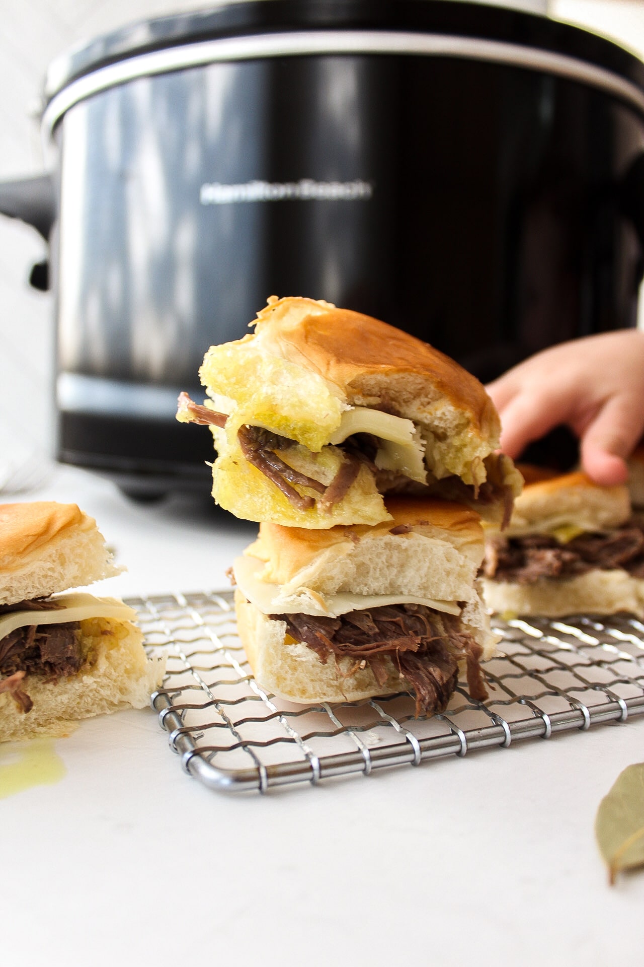 a stack of pot roast sliders with a hand grabbing another sandwich in the background
