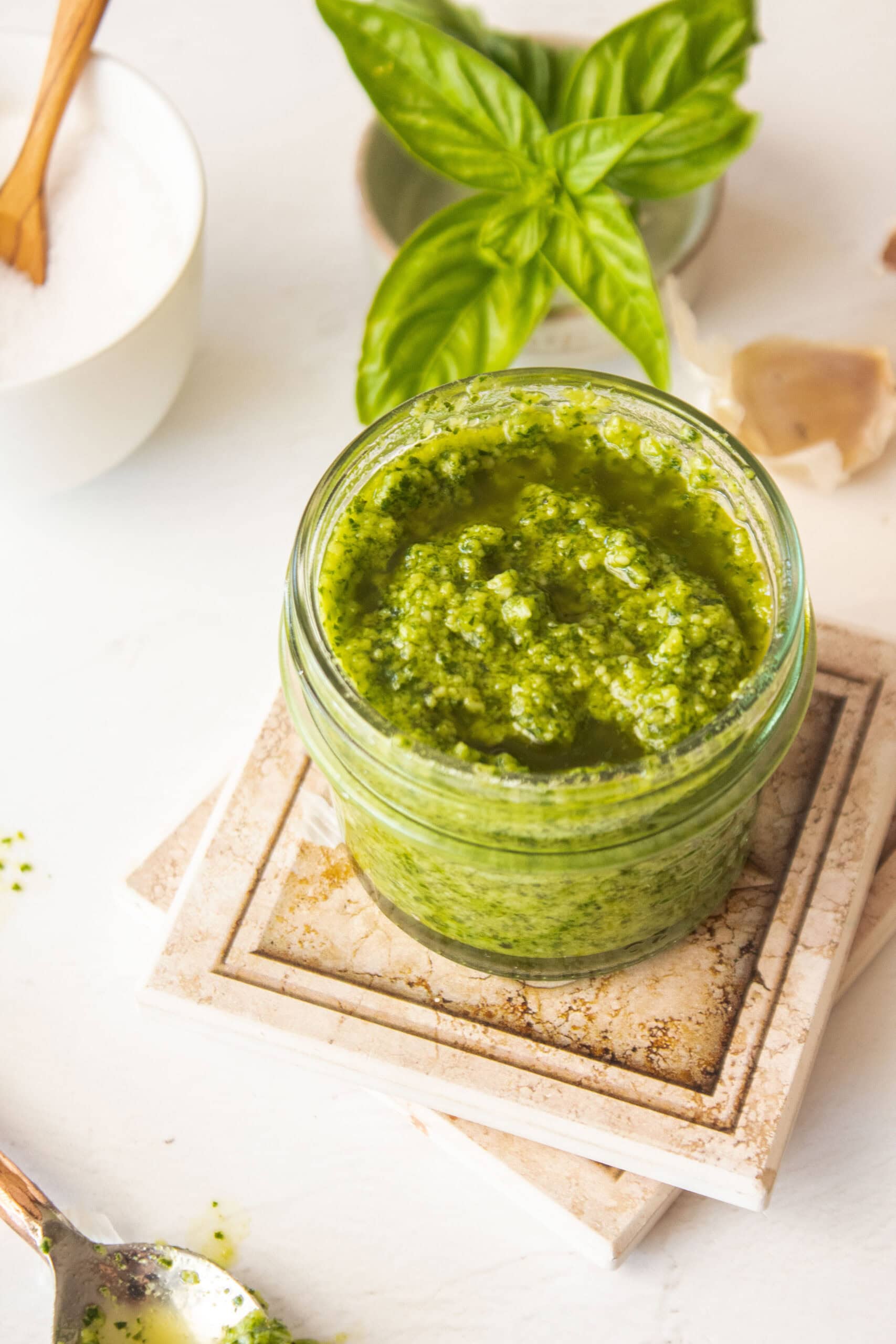 Nut free pesto in a glass jar with basil behind it and salt.