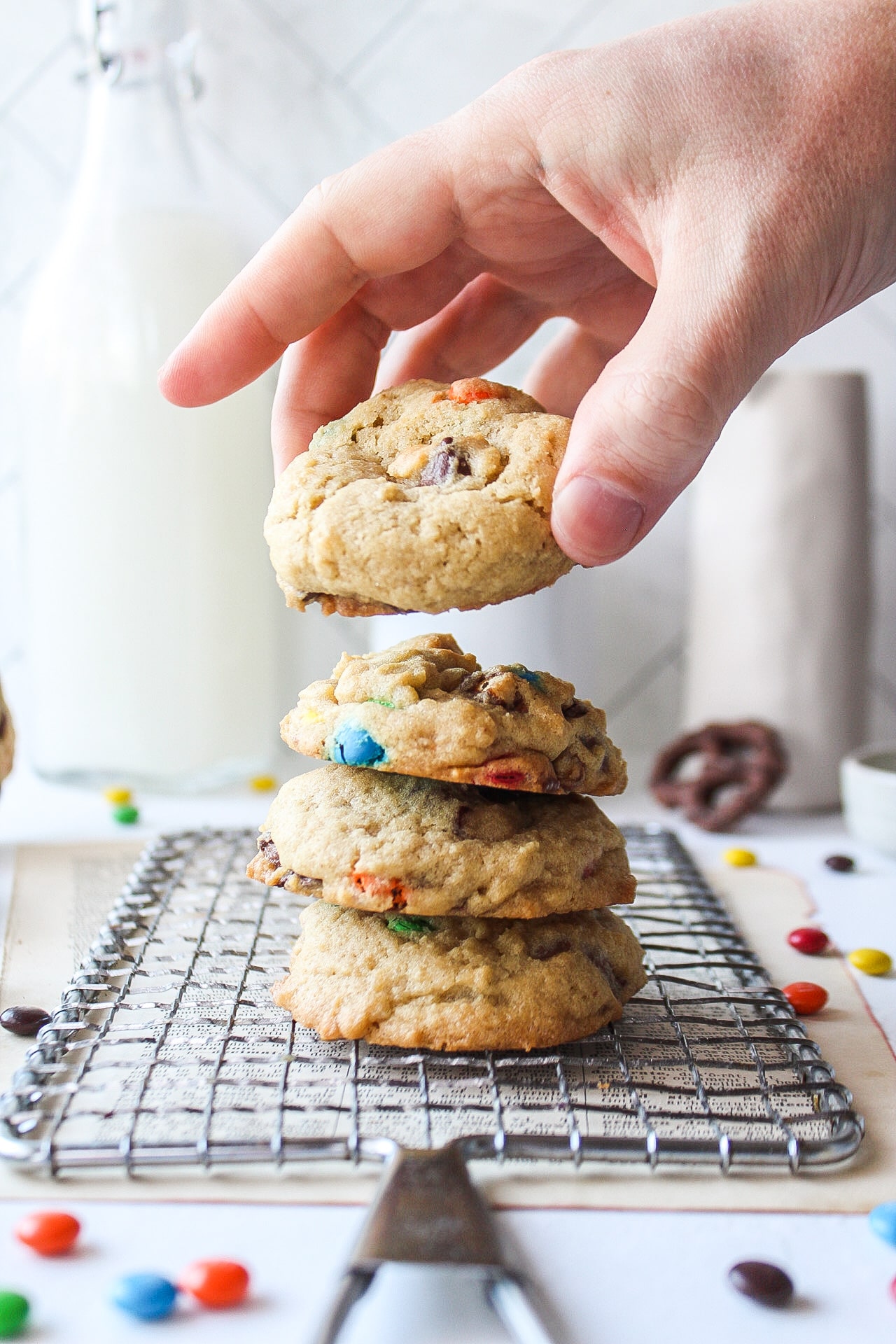 a stack of four cookies on a cooling rack with a hand grabbing the top cookie