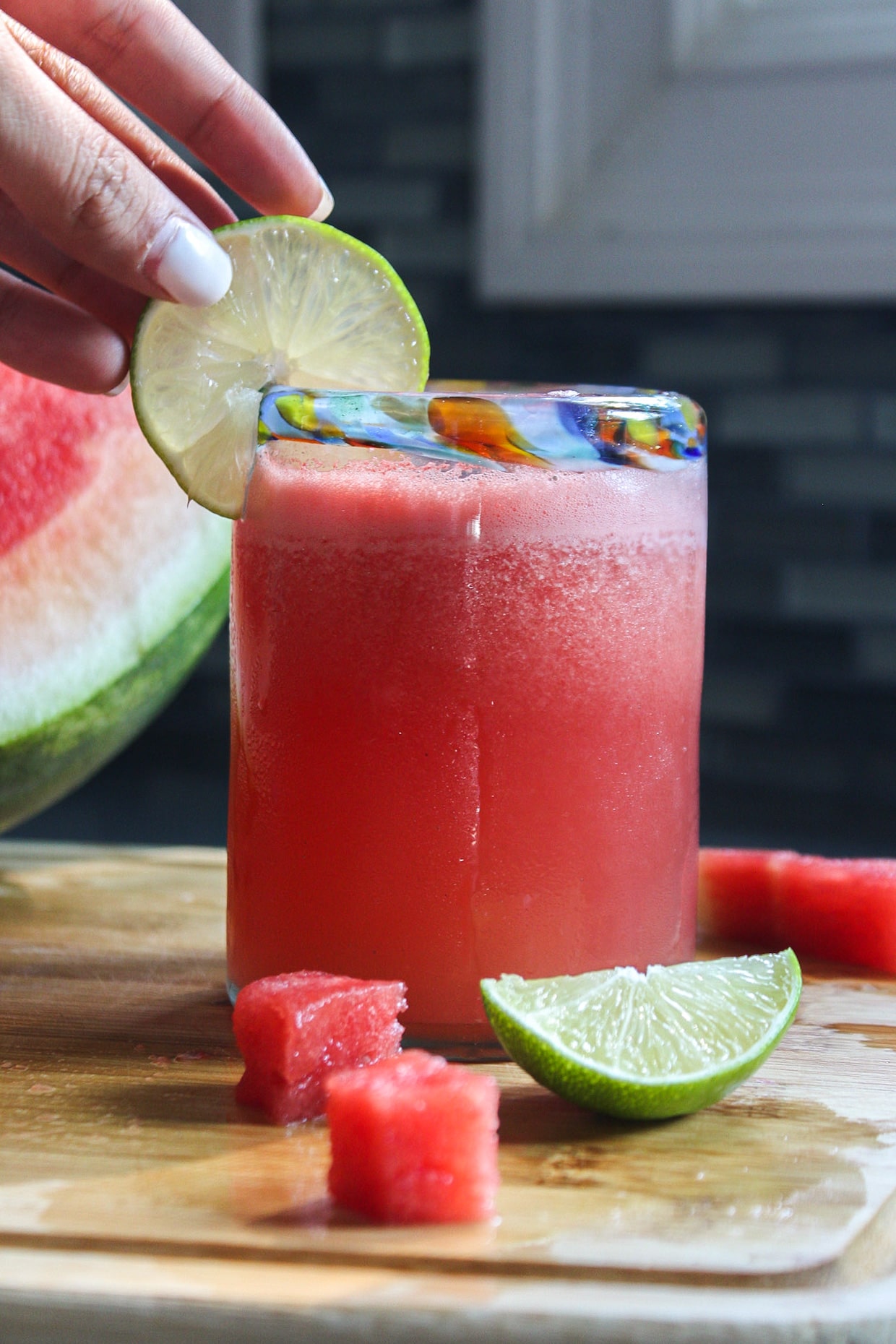 a glass of watermelon frose with a lime slice on the rim and a hand grabbing at the lime