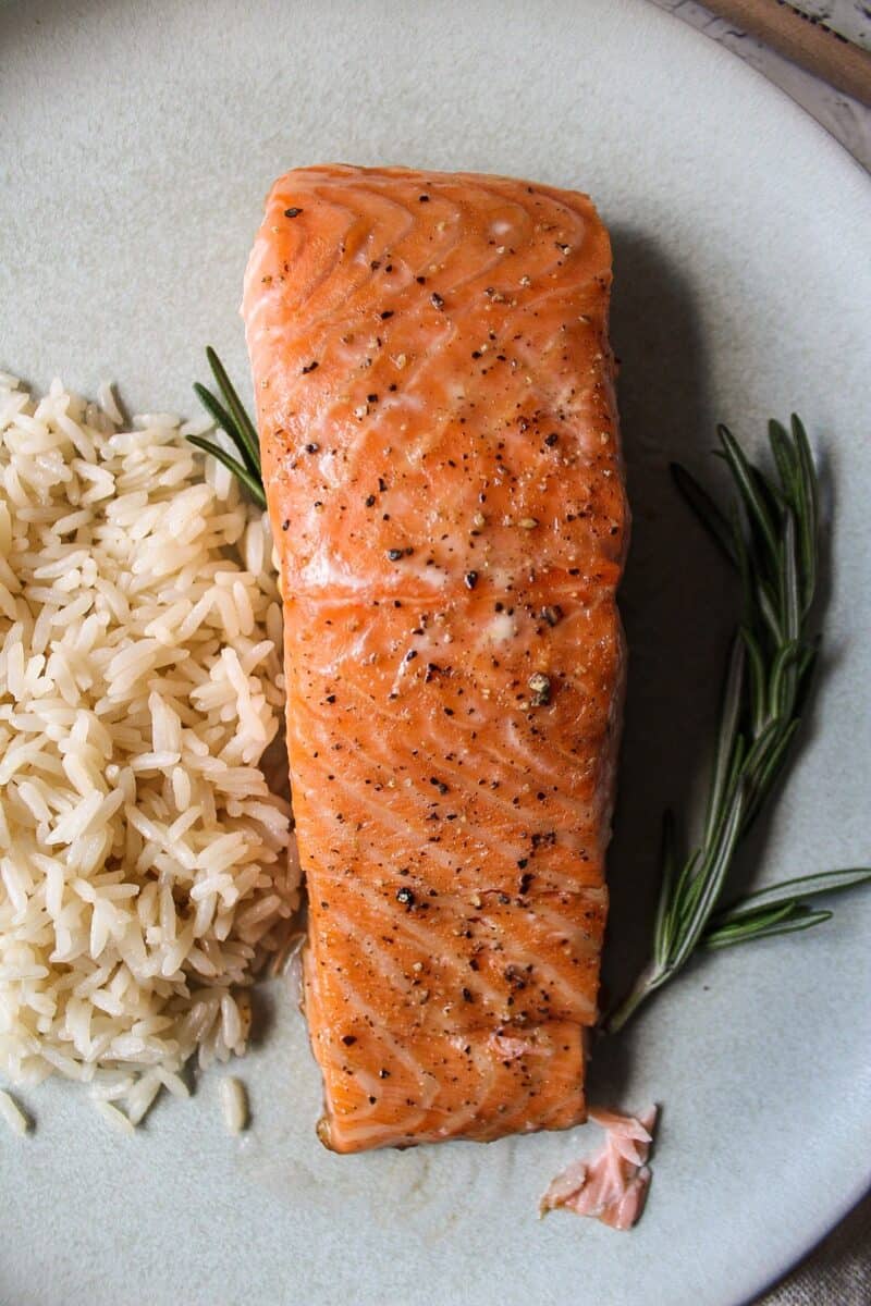a filet of salmon with rice and rosemary on a plate