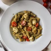 pesto, mozzarella, tomatoes, and pasta in a bowl mixed together.