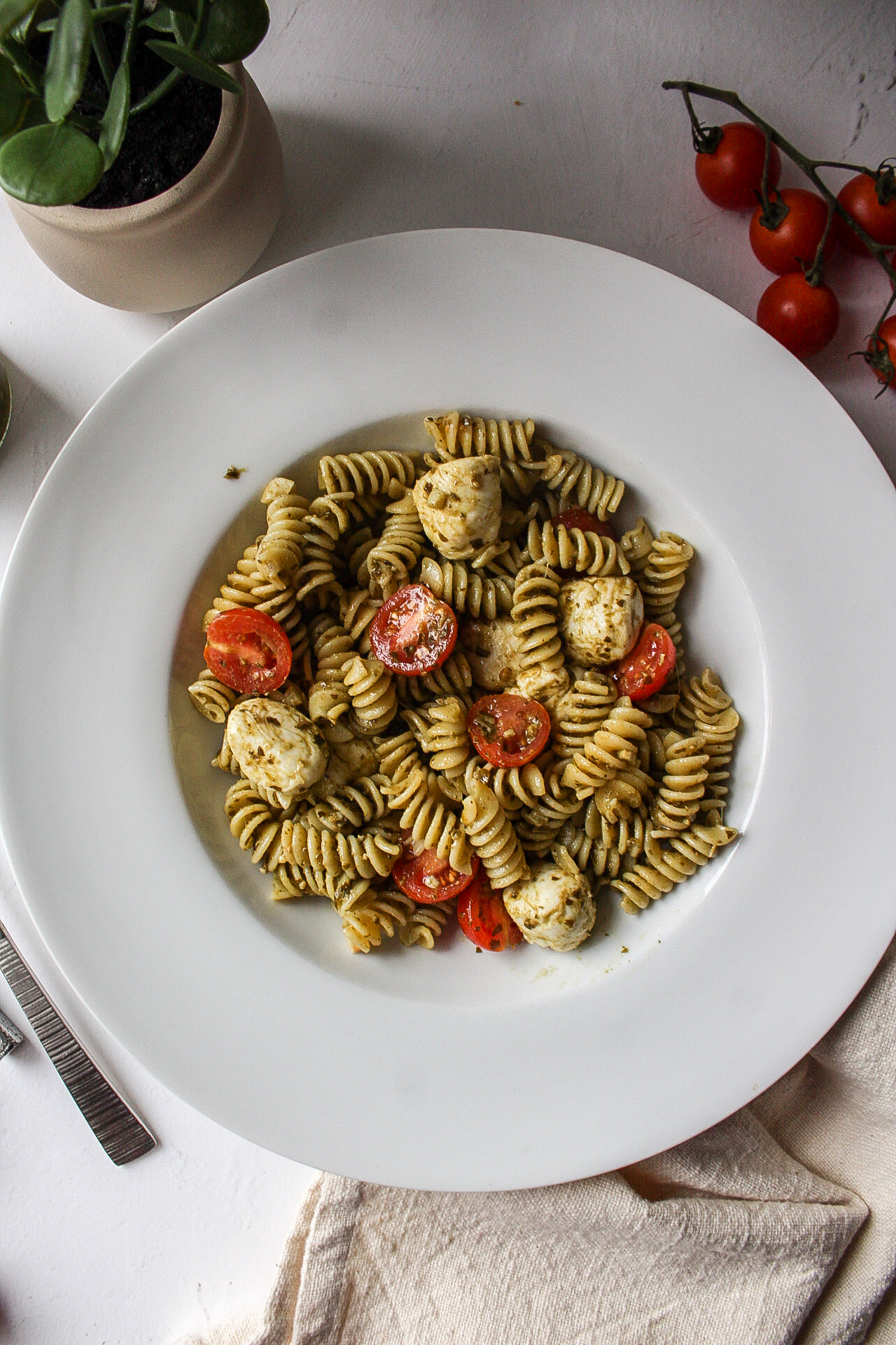 pesto, mozzarella, tomatoes, and pasta in a bowl mixed together.