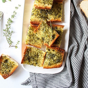 a plate of garlic bread with herbs around it