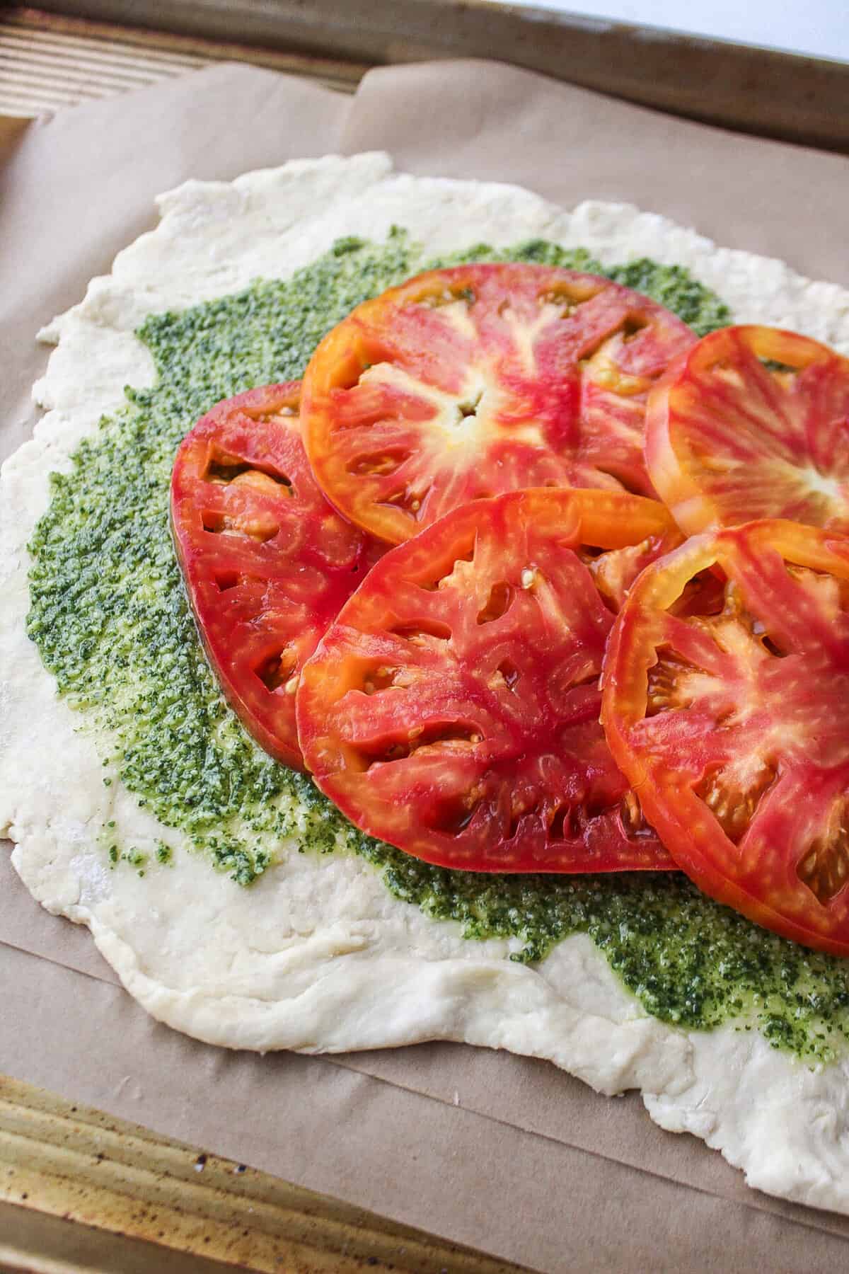 galette dough topped with pesto and sliced tomato