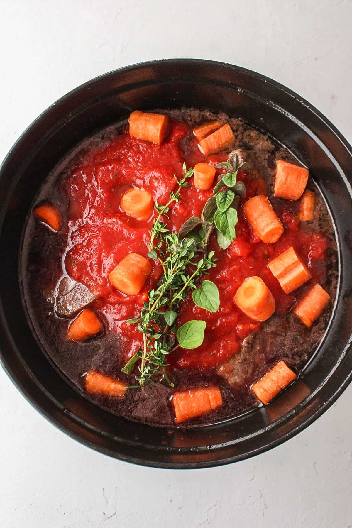 carrots, tomato sauce, and fresh herbs in a dutch oven with short ribs