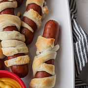 hot dogs wrapped and baked in crescent roll dough on a plate with mustard on the side