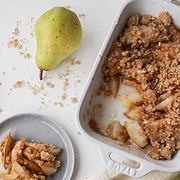 pear crumble in a baking dish with some crumble on a plate surrounded by pears