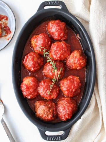 sweet and sour chicken meatballs in a black matte dish with thyme on top
