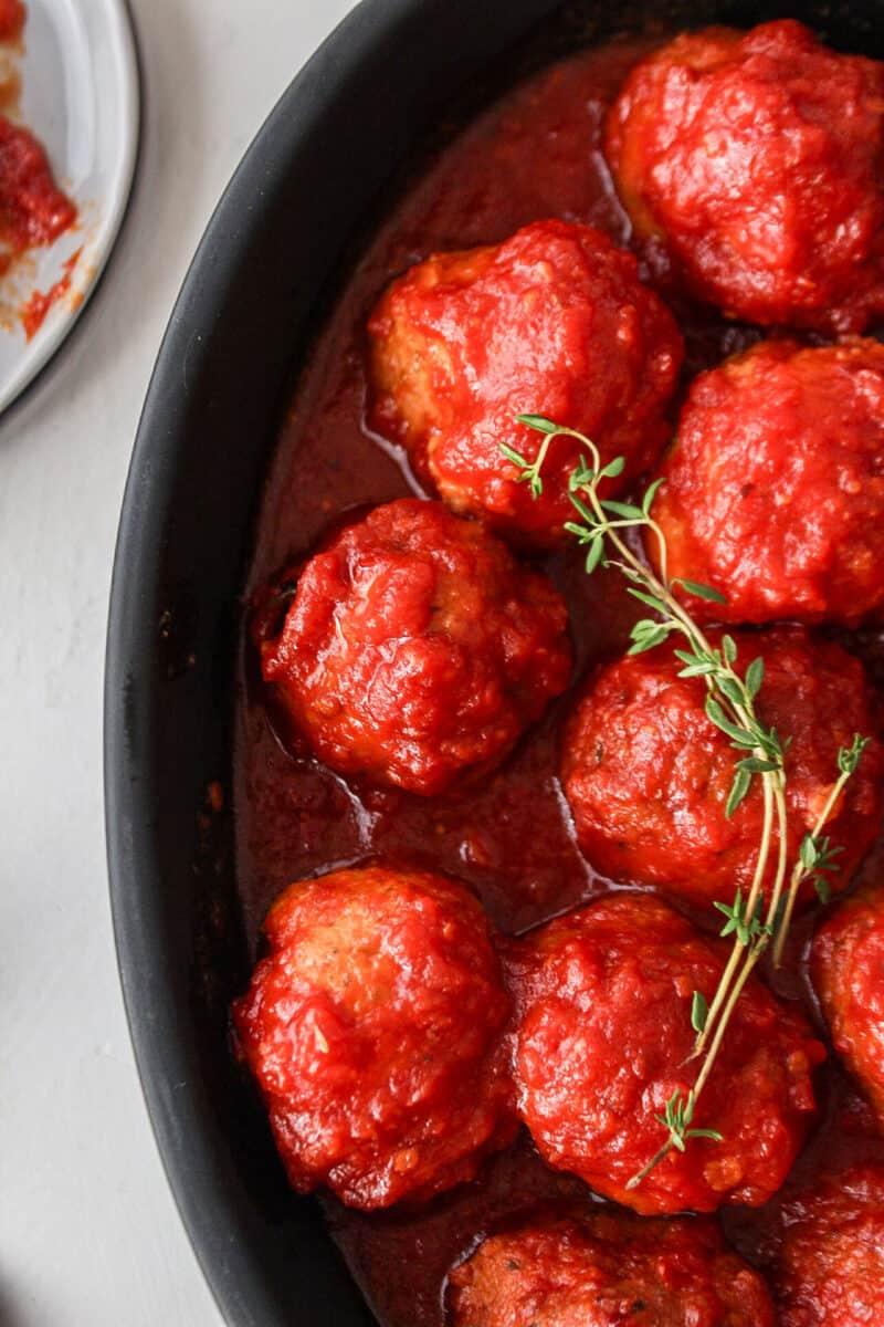 sweet and sour chicken meatballs in a black matte dish with thyme on top