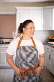 morgan standing with an apron on in the kitchen turning her head to the side and smiling