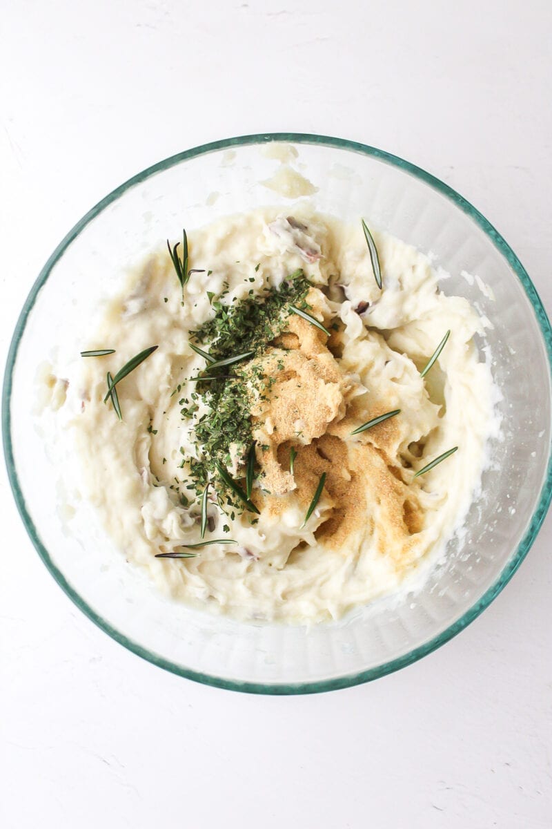 garlic, parsley, and rosemary added to a bowl of mashed potatoes