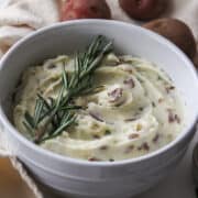 creamy garlic and herb red mashed potatoes in a bowl with rosemary on top