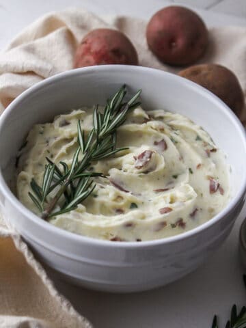 creamy garlic and herb red mashed potatoes in a bowl with rosemary on top