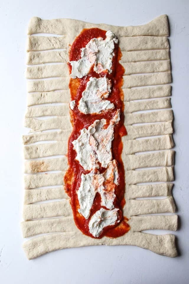 pizza crust on a surface with small slits on the sides with the inside filled with marinara and ricotta