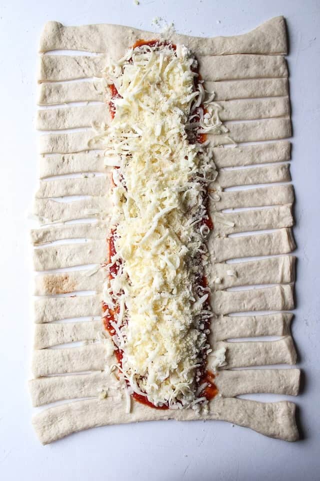 pizza crust on a surface with small slits on the sides with the inside filled with marinara and ricotta and cheese