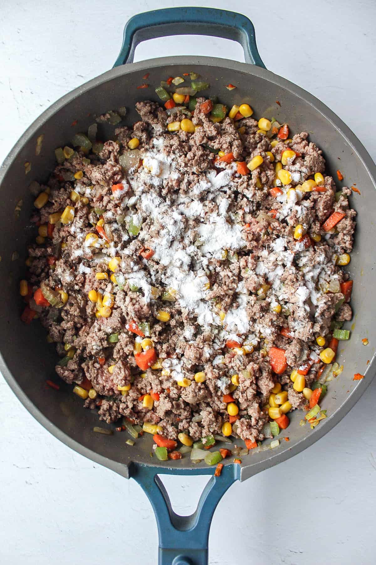 shepherd's pie vegetables and ground beef with flour sprinkled on top.