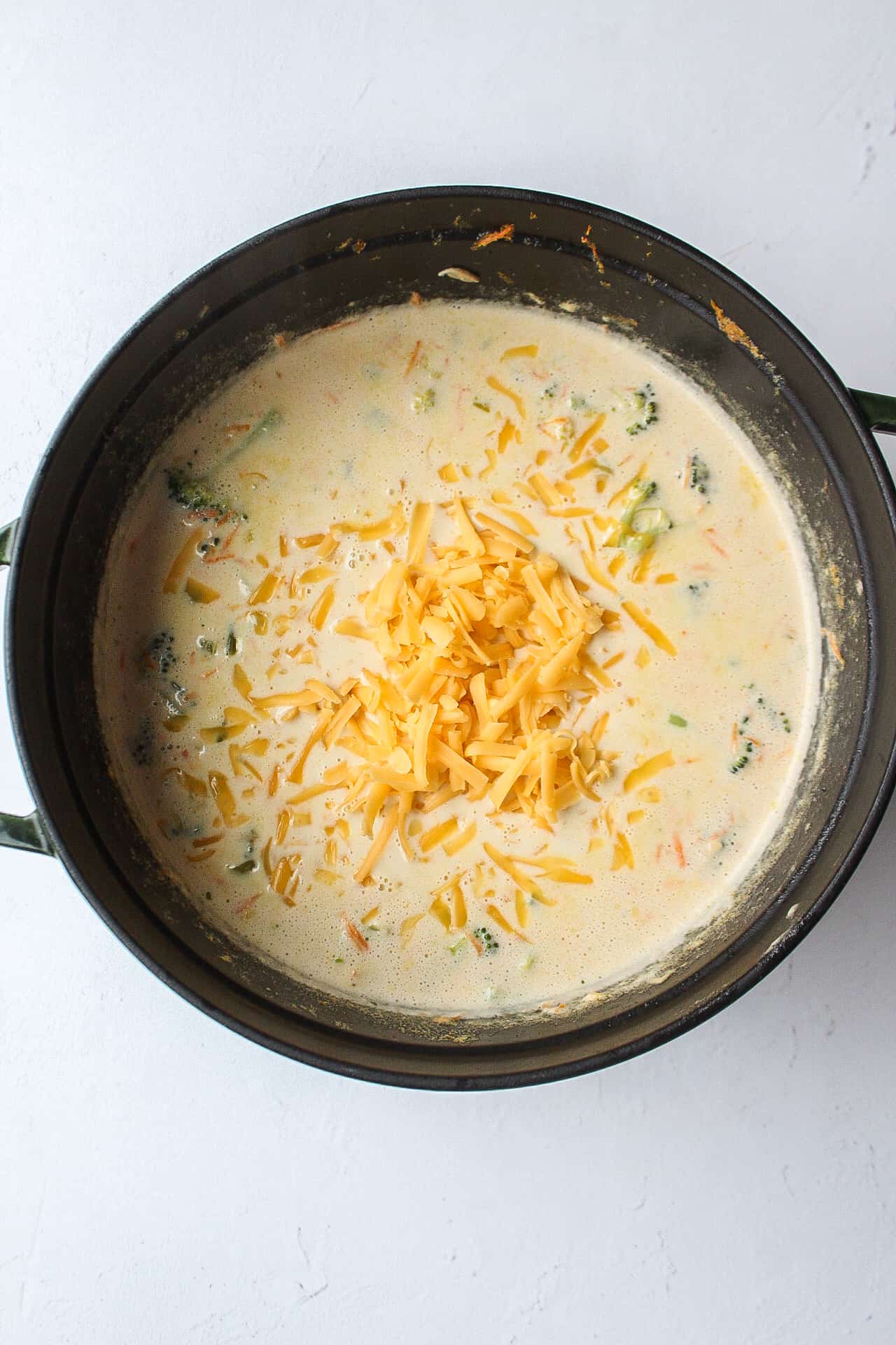 cheddar cheese added to a pot of broccoli cheddar soup.