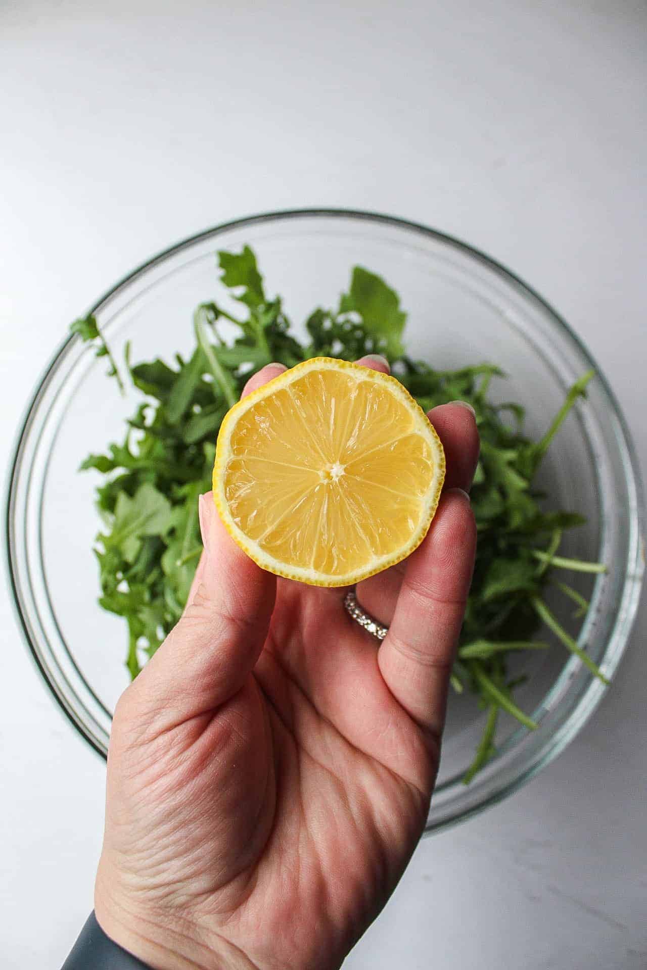 arugula lettuce in a large bowl with a half of a lemon in a hand.