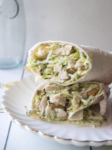 A chicken caesar wrap stacked on top of each other on a white scalloped plate.