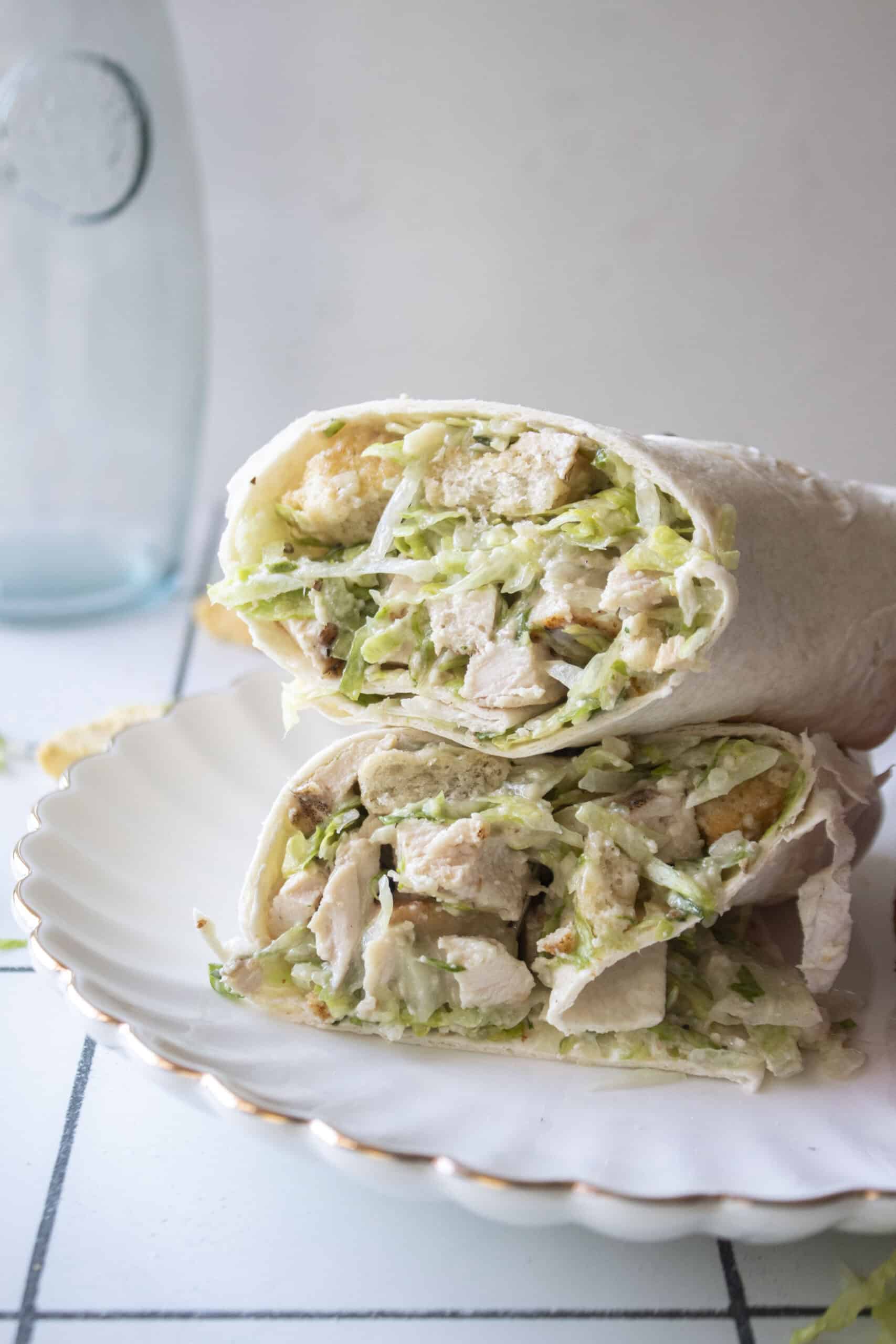 A chicken caesar wrap stacked on top of each other on a white scalloped plate.