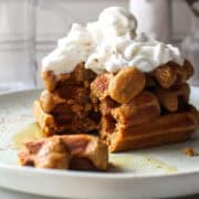 a stack of three gingerbread waffles topped with whipped cream.