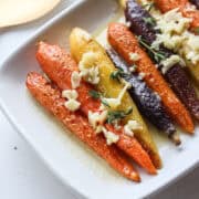 garlic butter rainbow roasted carrots on a plate with garlic and thyme on top.