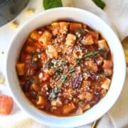 minestrone soup with parmesan and thyme on top in a bowl.