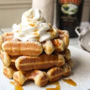 A stack of three baileys waffles on a plate with whipped cream and syrup.
