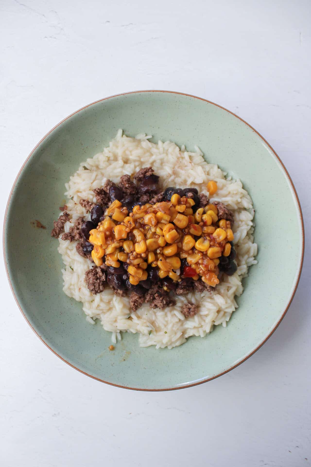 Corn salsa on top of ground beef and black beans in a rice bowl.