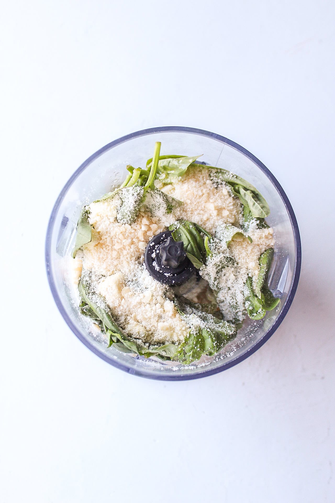 Ingredients such as basil, parmesan cheese, olive oil, and garlic to make homemade pesto in a food processor