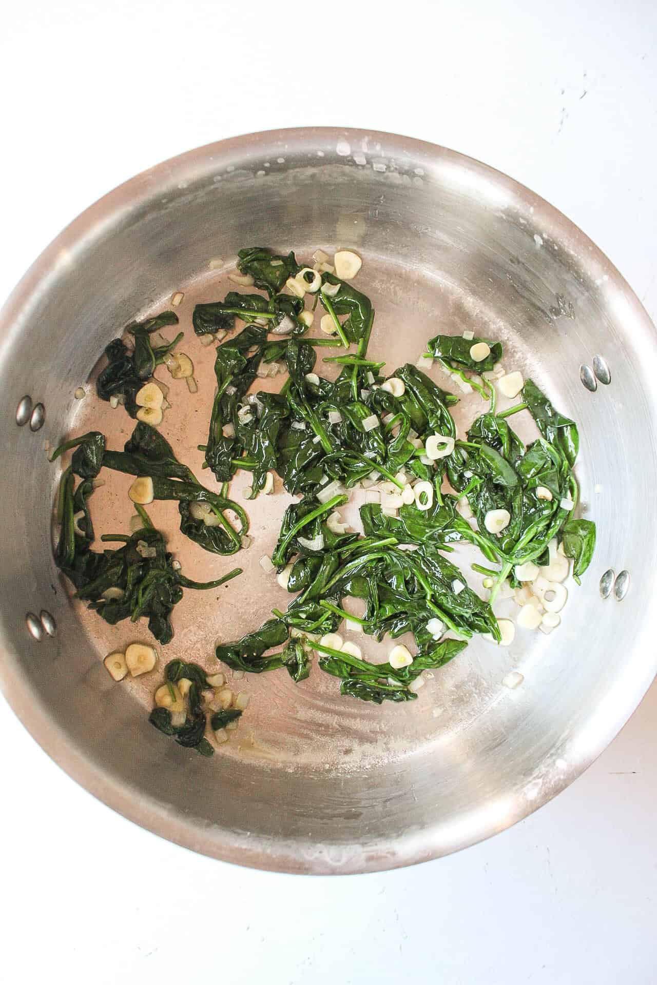 Saut&eacute;ed spinach with garlic and shallot in a large pot.