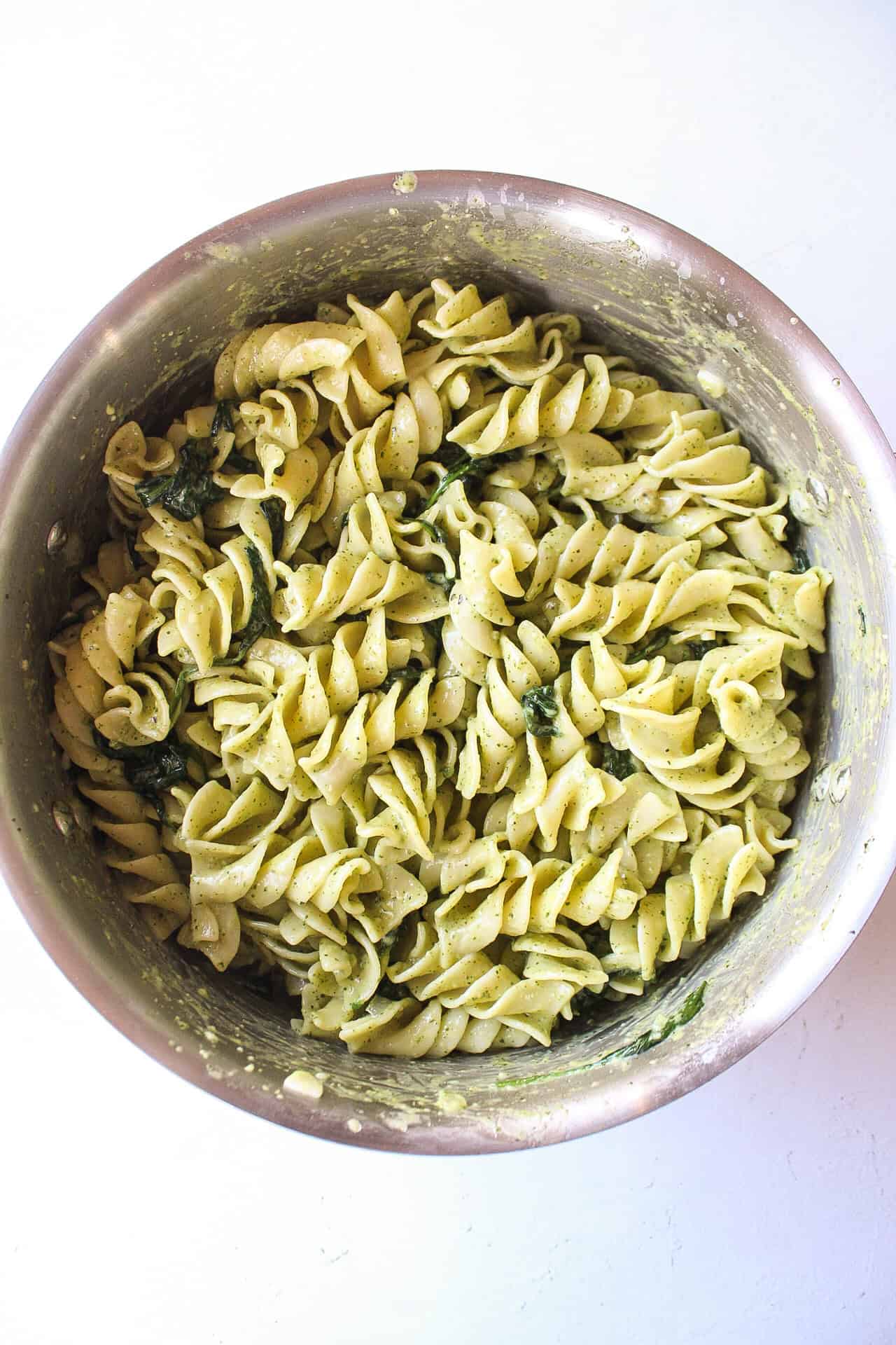 Pasta mixed with pesto and spinach in a pot.
