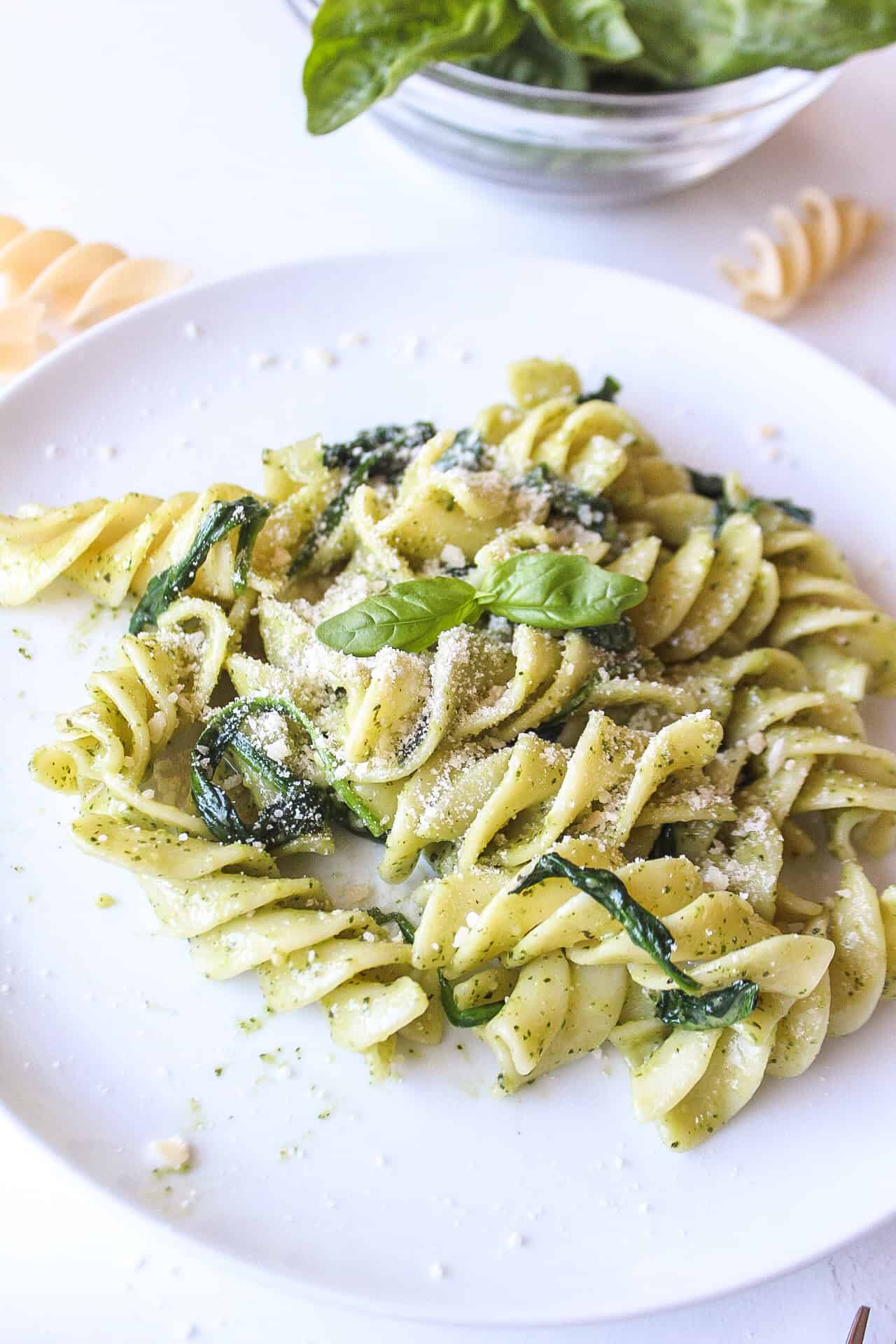 Pasta mixed with pesto and spinach on a plate with parmesan cheese.