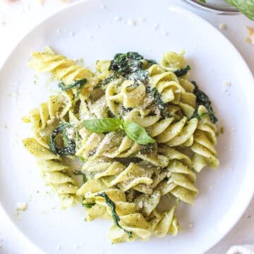 Pasta mixed with pesto and spinach on a plate with parmesan cheese.