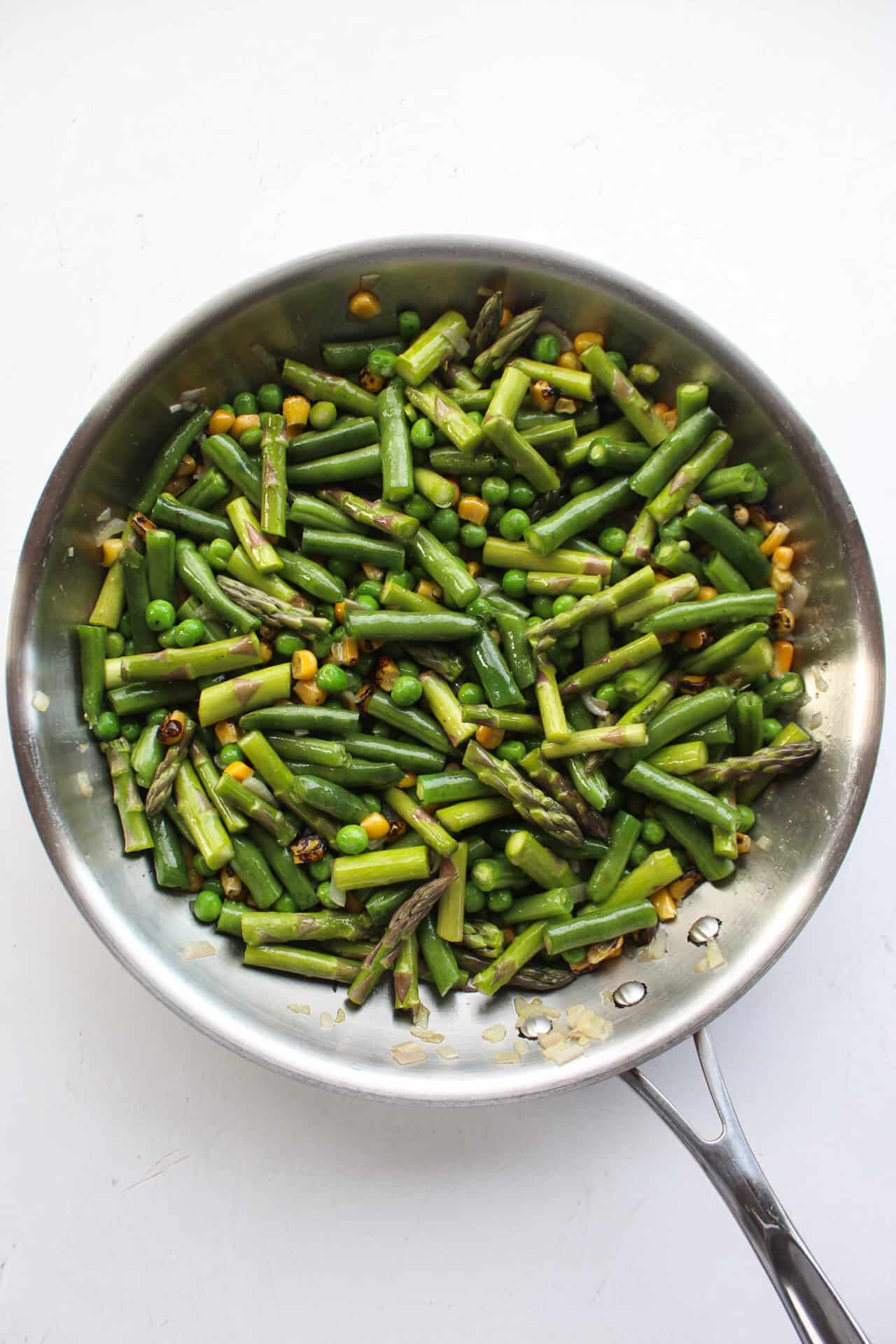 Corn, peas, green beans, and asparagus in a large saute pan with shallot and olive oil.