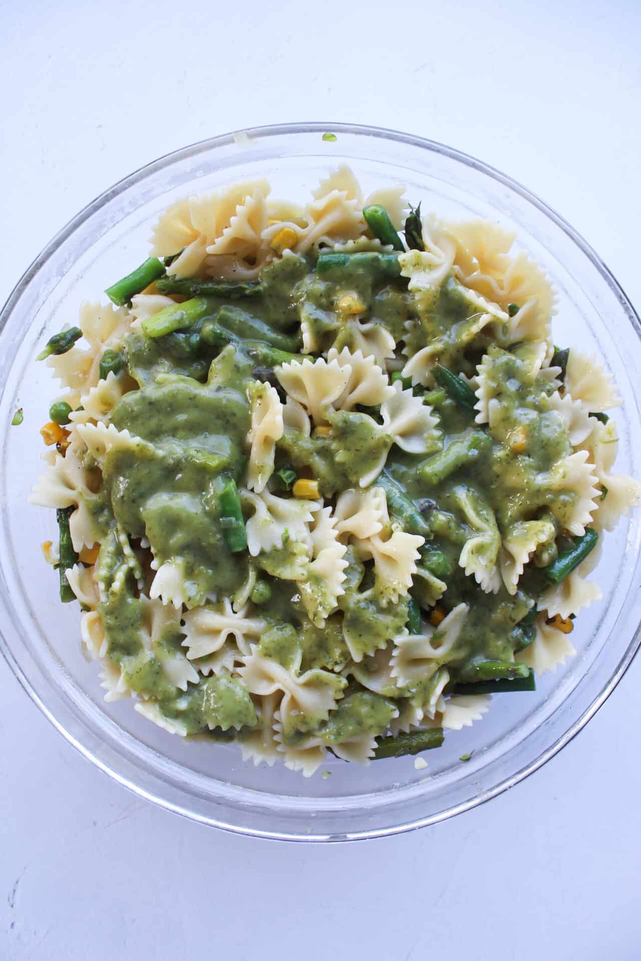 Green goddess dressing added to a bowl of pasta with sauteed vegetables.