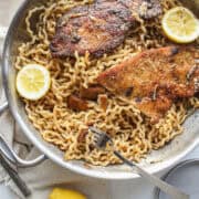 Chicken cutlets on top of a bed of pasta in a garlic, butter, lemon sauce.