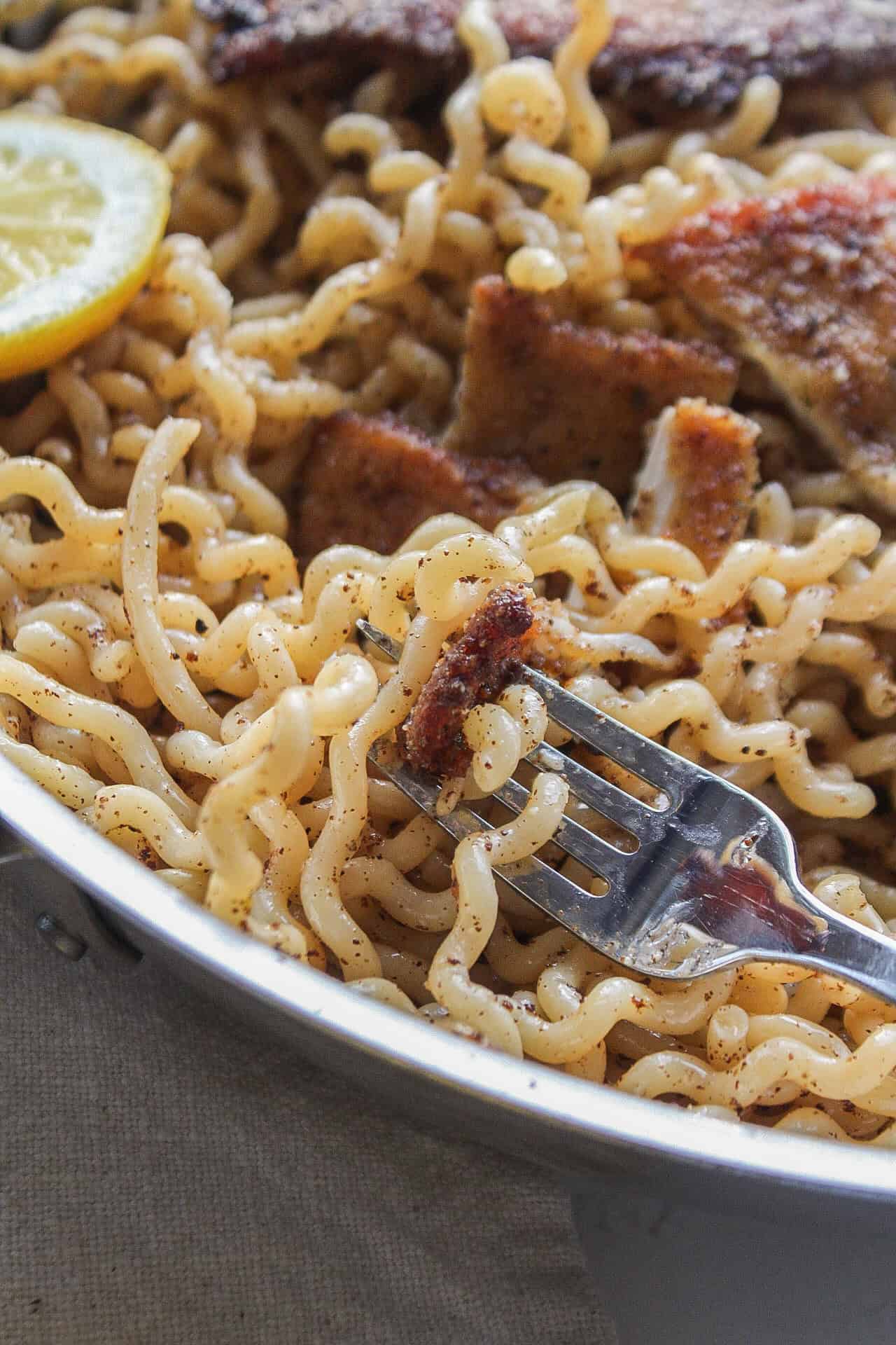 Close up of a forkful of pasta with chicken cutlet in a frying pan.