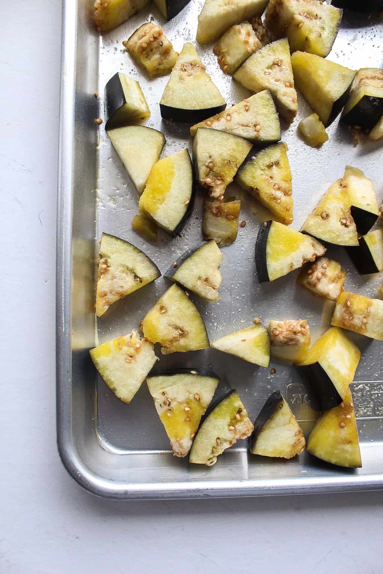 Diced eggplant on a baking sheet with olive oil and salt.