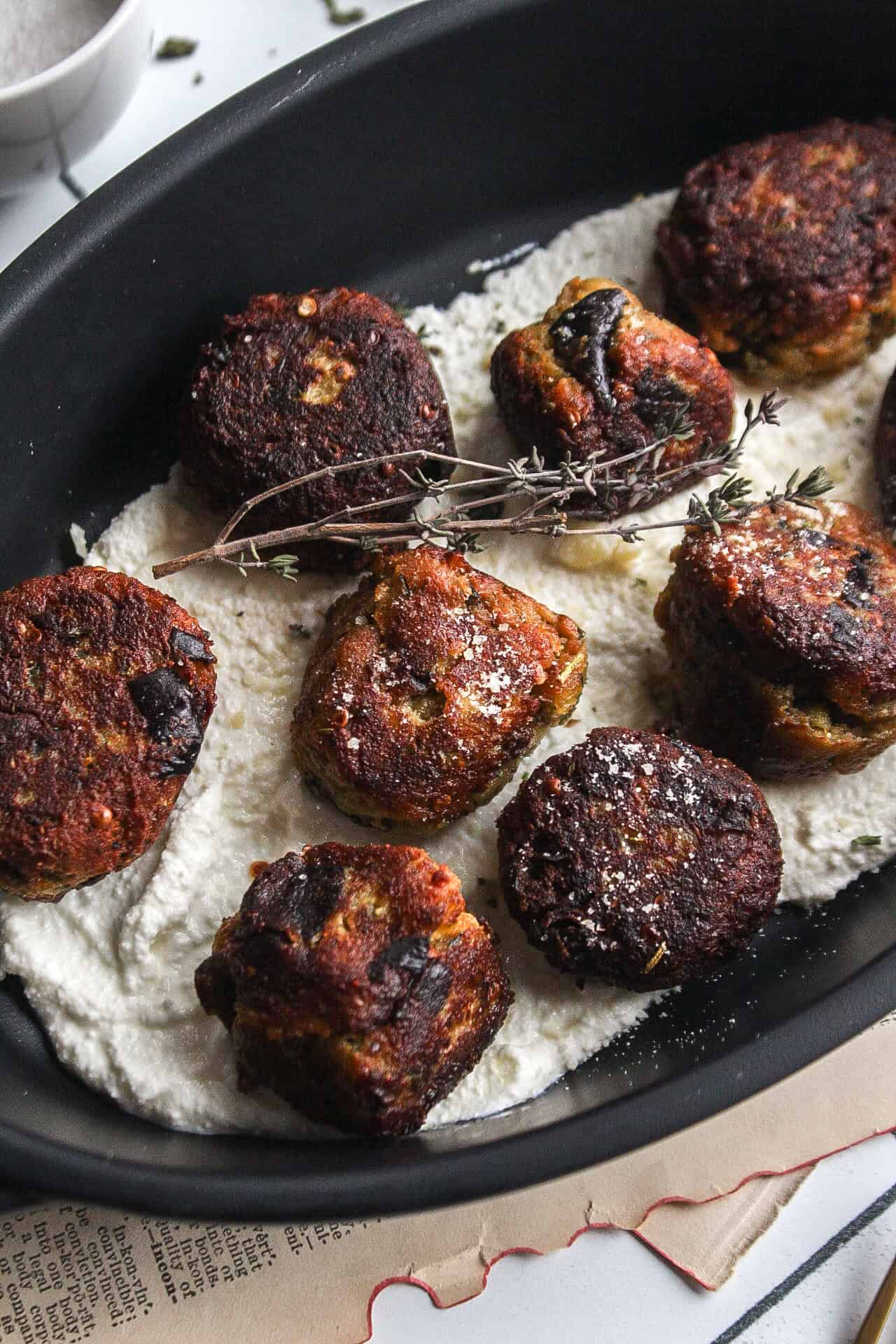 Several eggplant and ricotta meatballs on a bed of ricotta topped with fresh thyme and parmesan cheese.