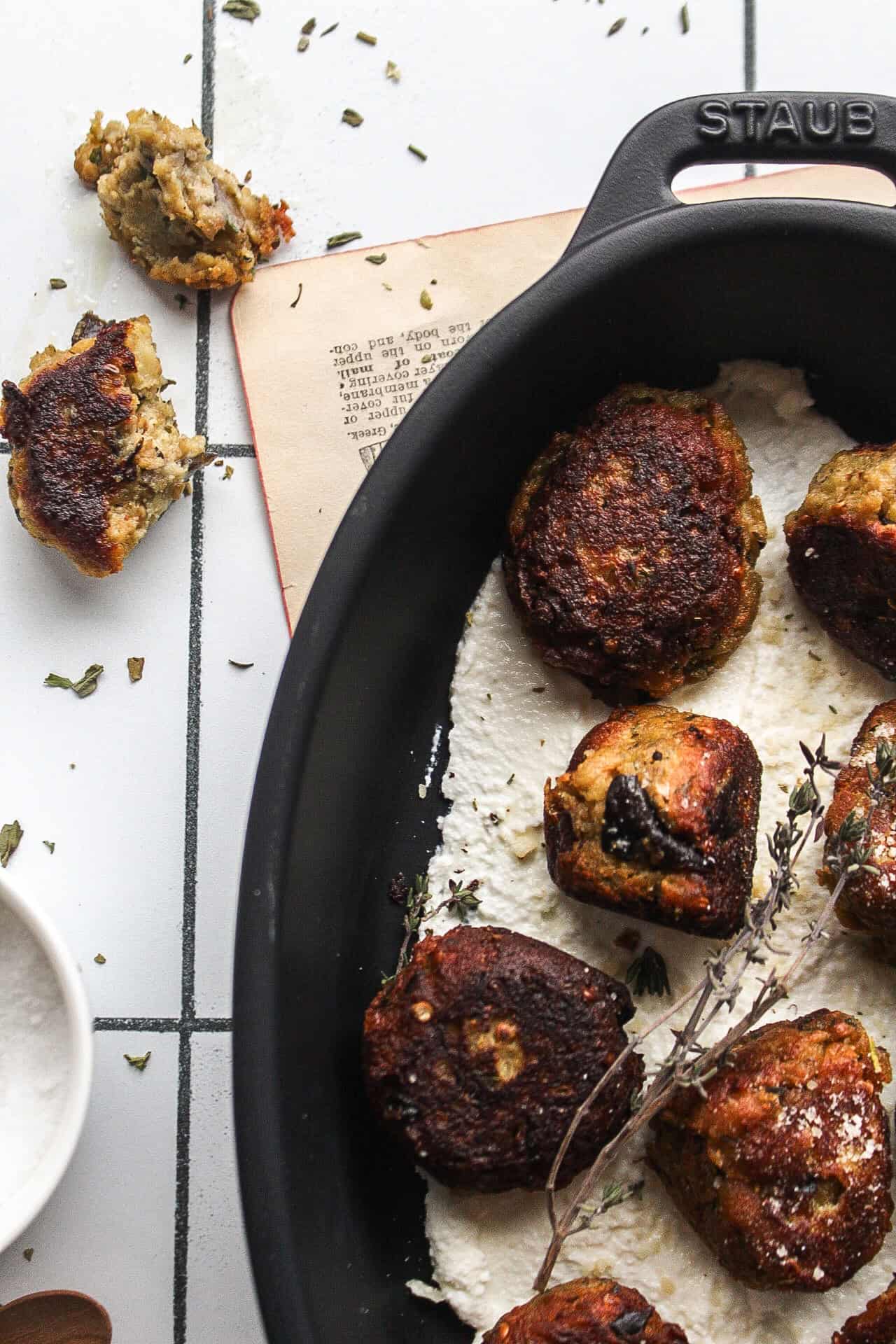 Several eggplant and ricotta meatballs on a bed of ricotta topped with fresh thyme and parmesan cheese.
