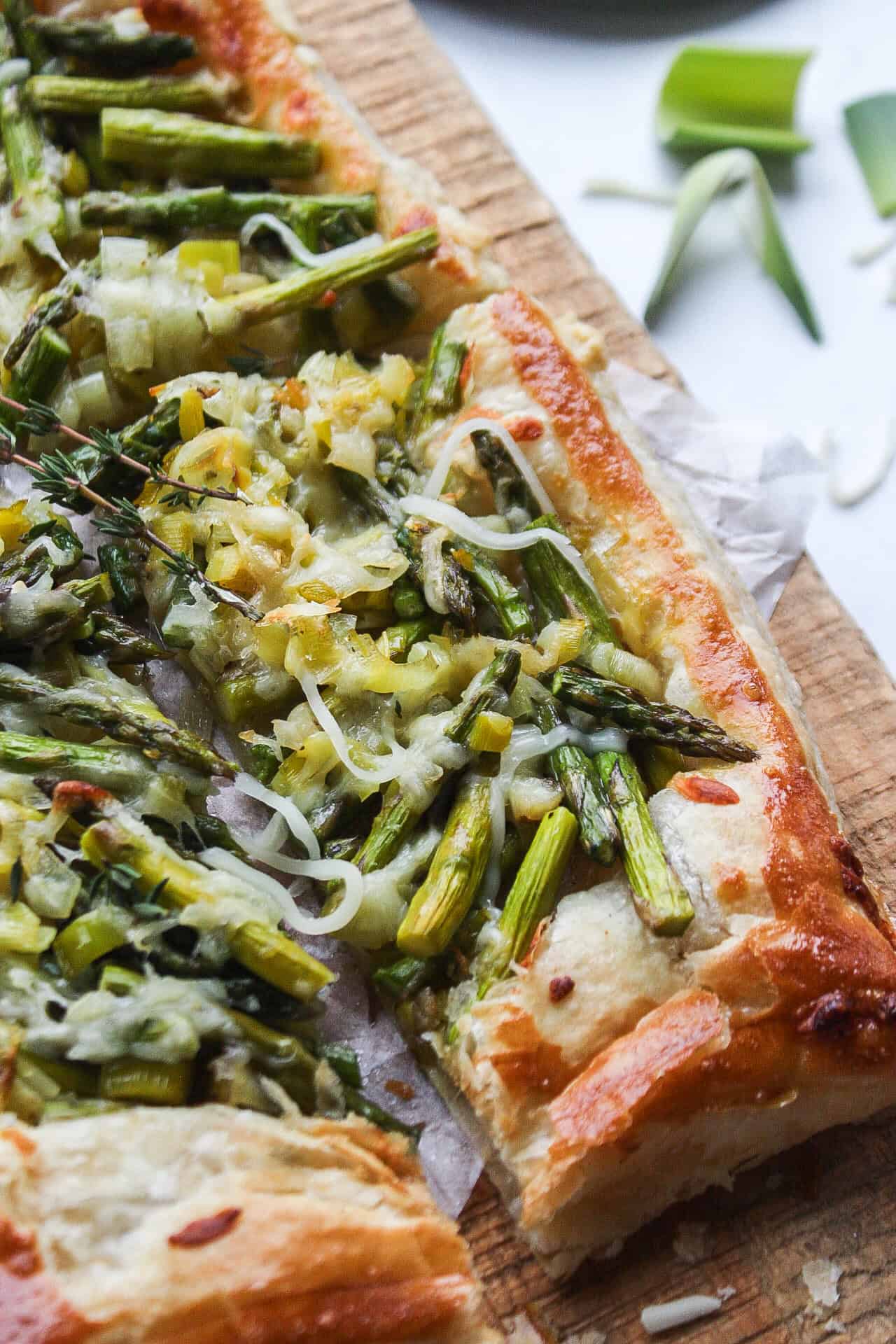 An asparagus and leek tart on cutting board with parchment paper.