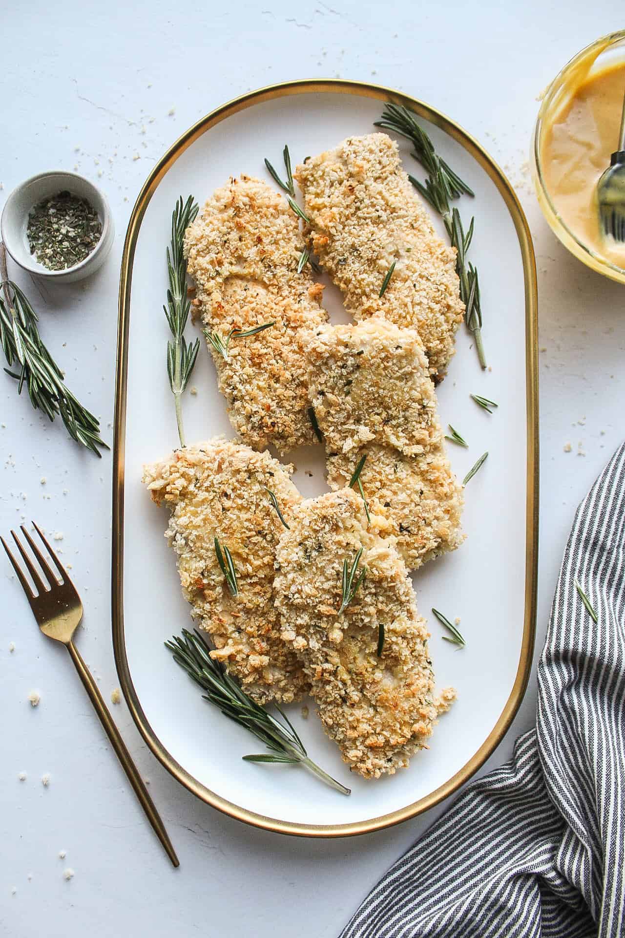 Panko honey mustard chicken on a serving platter with rosemary.