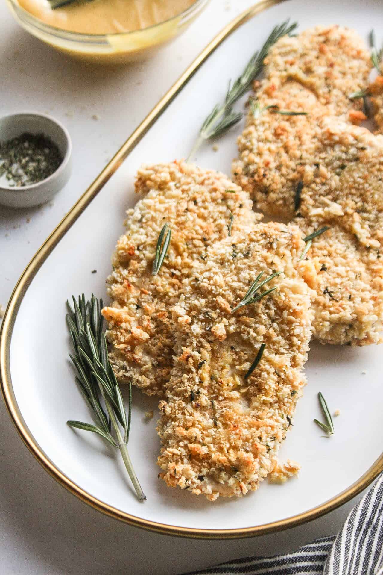 Panko honey mustard chicken on a serving platter with rosemary.