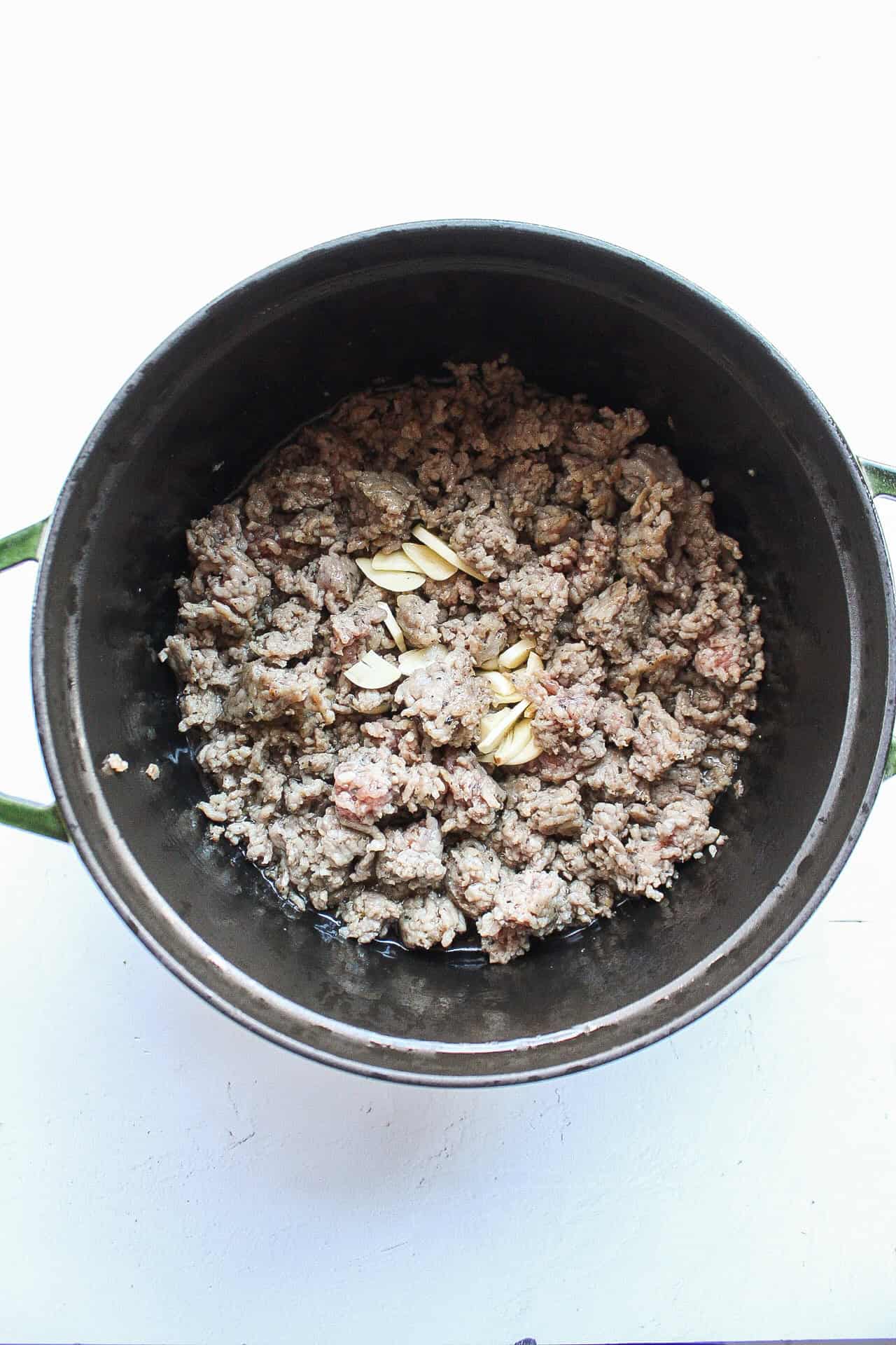 Browned ground pork sausage in a dutch oven with garlic.