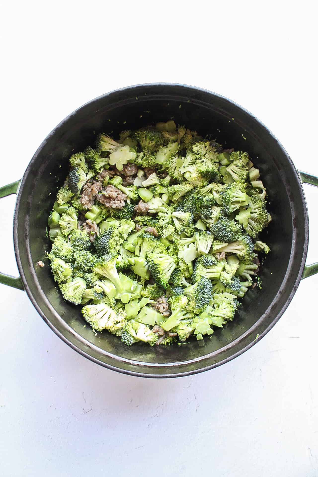 Fresh broccoli added to ground sausage in a dutch oven.